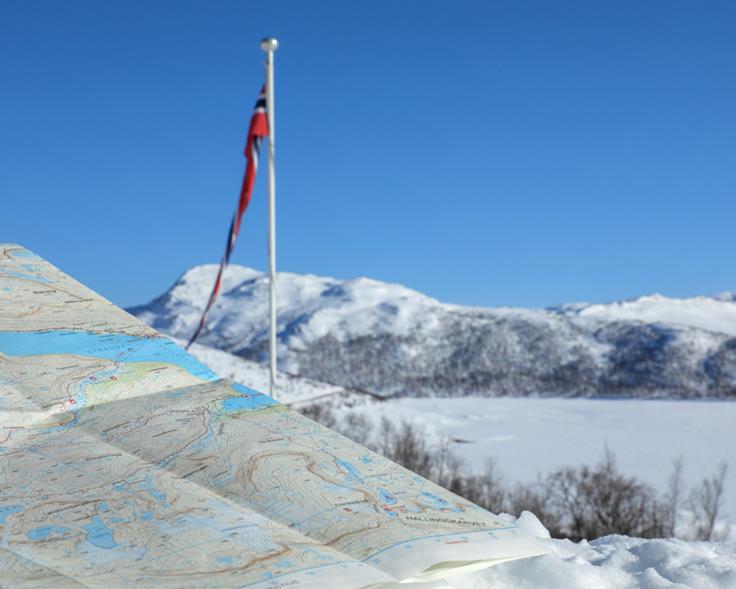 Topografisk kart foran flaggstang og snødekt vinterlandskap. Foto: Per Anders Bjørklund/ Kartverket
