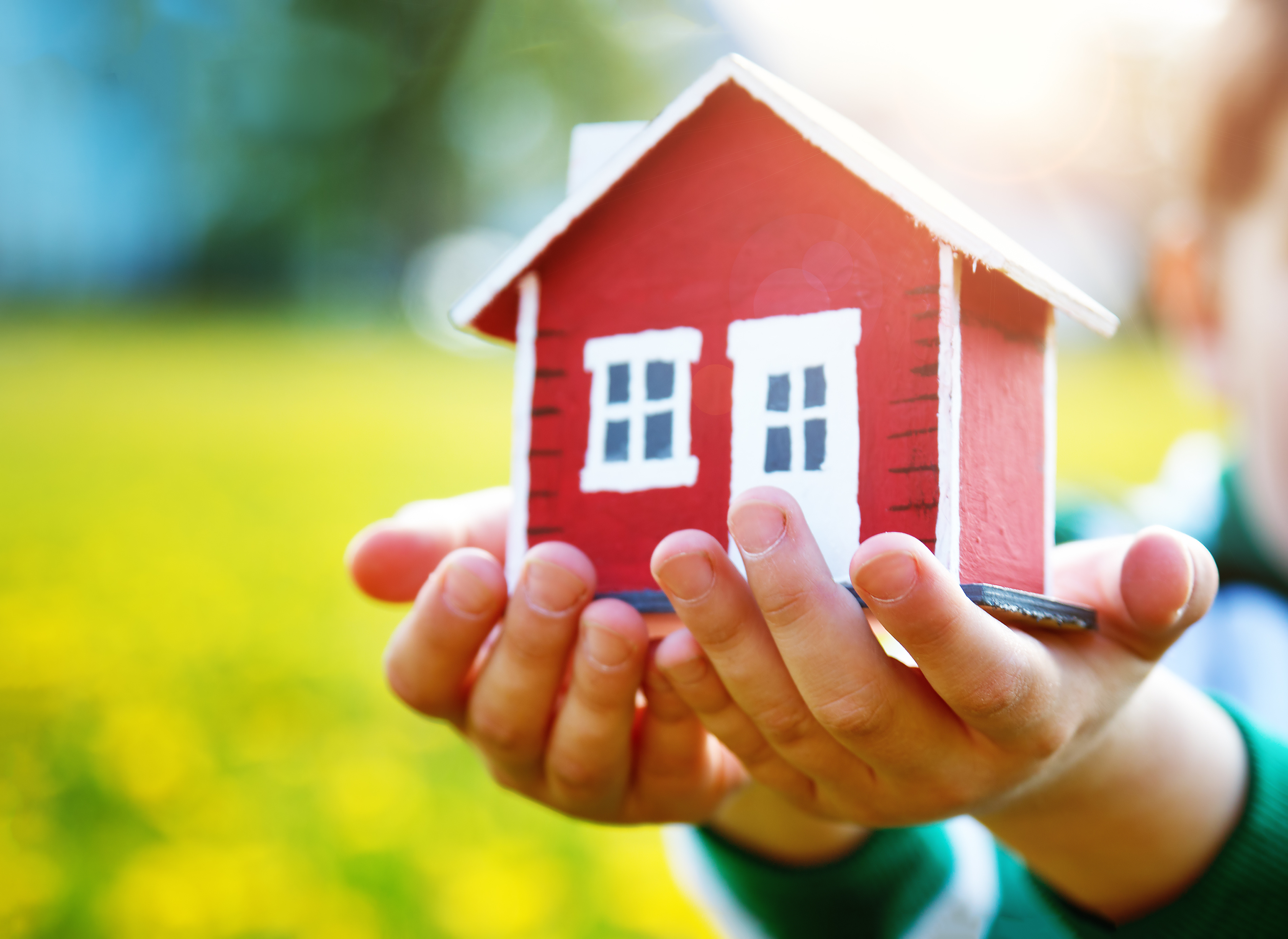 To små barnehender holder en modell av et lite, rødt hus.