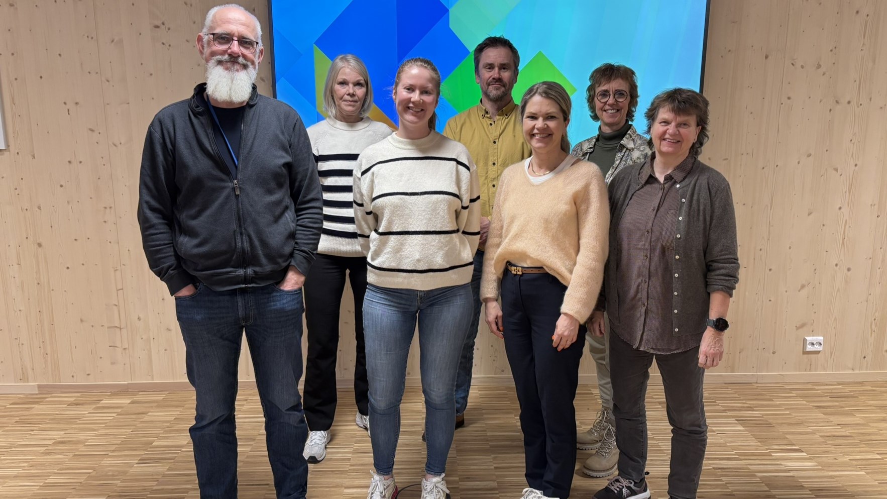 To menn og fem kvinner st&aring;r foran en innend&oslash;rs vegg