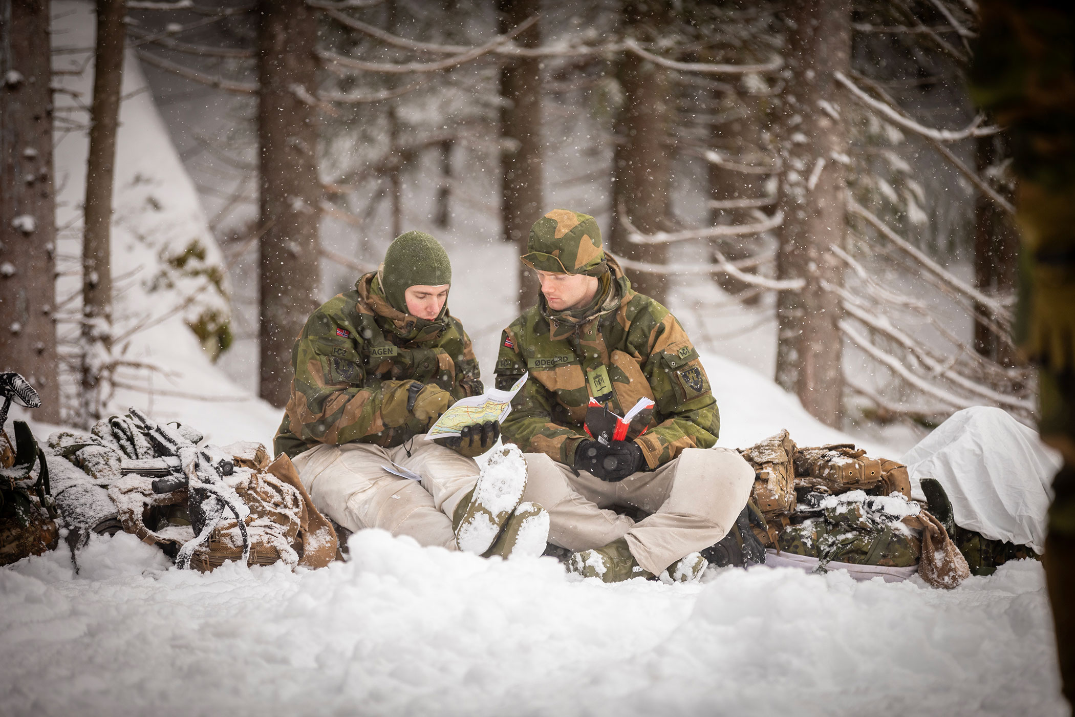 To soldater sitter i vinterskog p&aring; en pulk og kikker p&aring; kart
