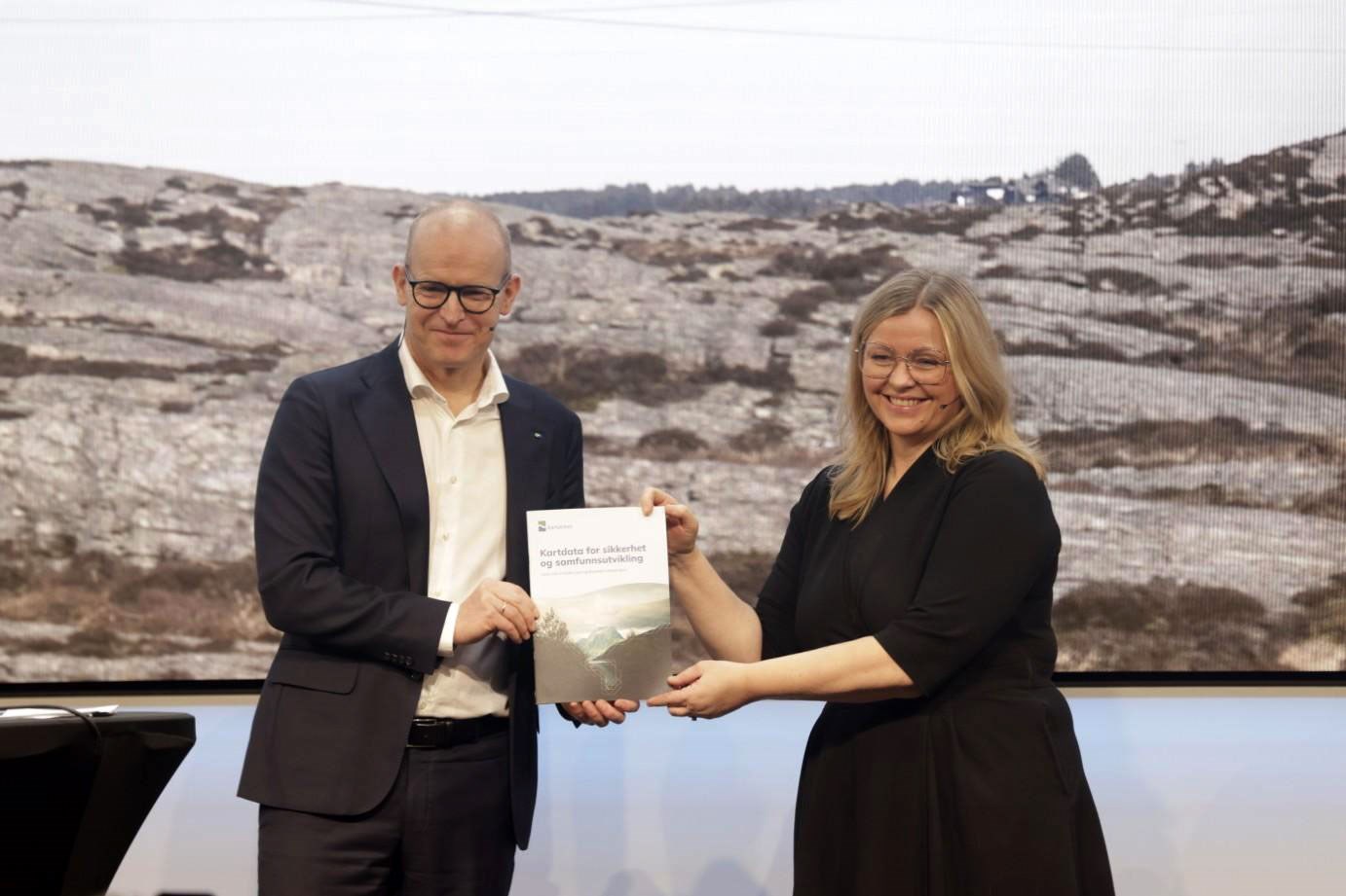 Kvinnelig statsr&aring;d mottar Kartverkets statusrapport fra mannlig kartverkssjef p&aring; et podium