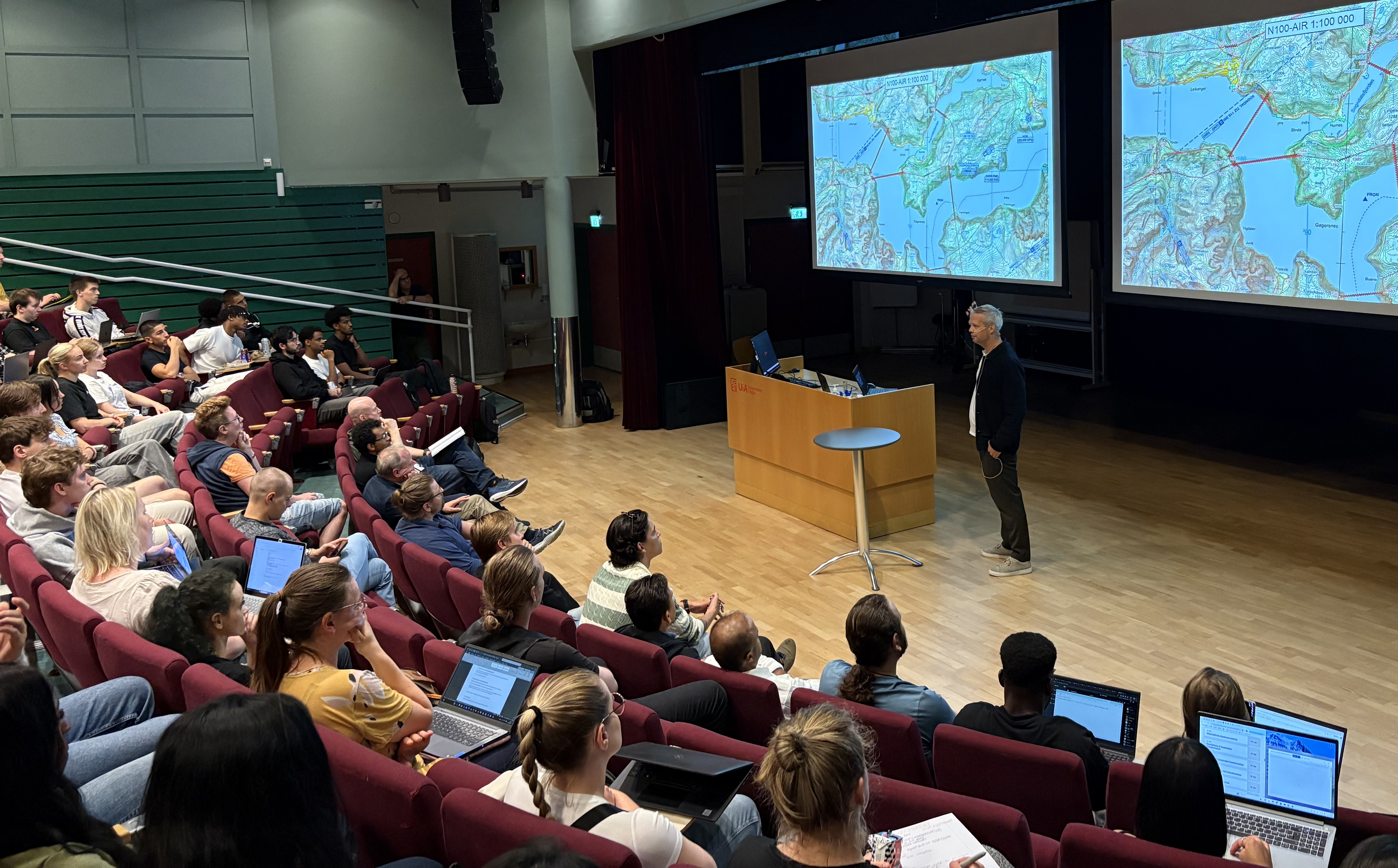 Mannlig fylkeskartsjef foran forsamling med studenter som ser p&aring; et kart p&aring; storskjerm.