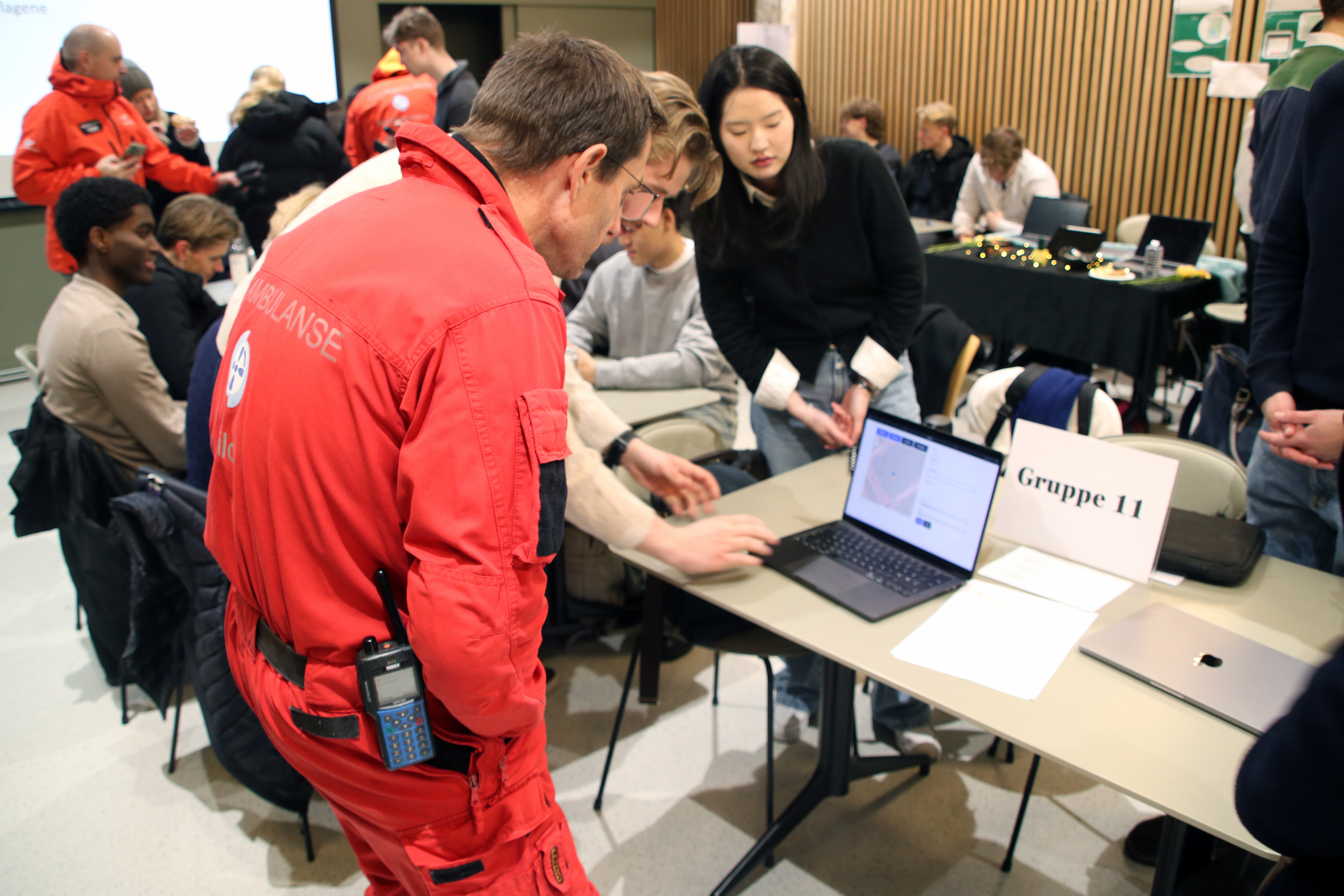 Et tredimensjonEn mannlig helikopterpilot fra Norsk Luftambulanse studerer ivrig en PC-skjerm sammen med studenter. Foto: Magnus Nødland Skogedal/ Universitetet i Agderalt bilda av sentrumsområder i Trondheim laga fra detaljerte FKB-data i 2,5D.