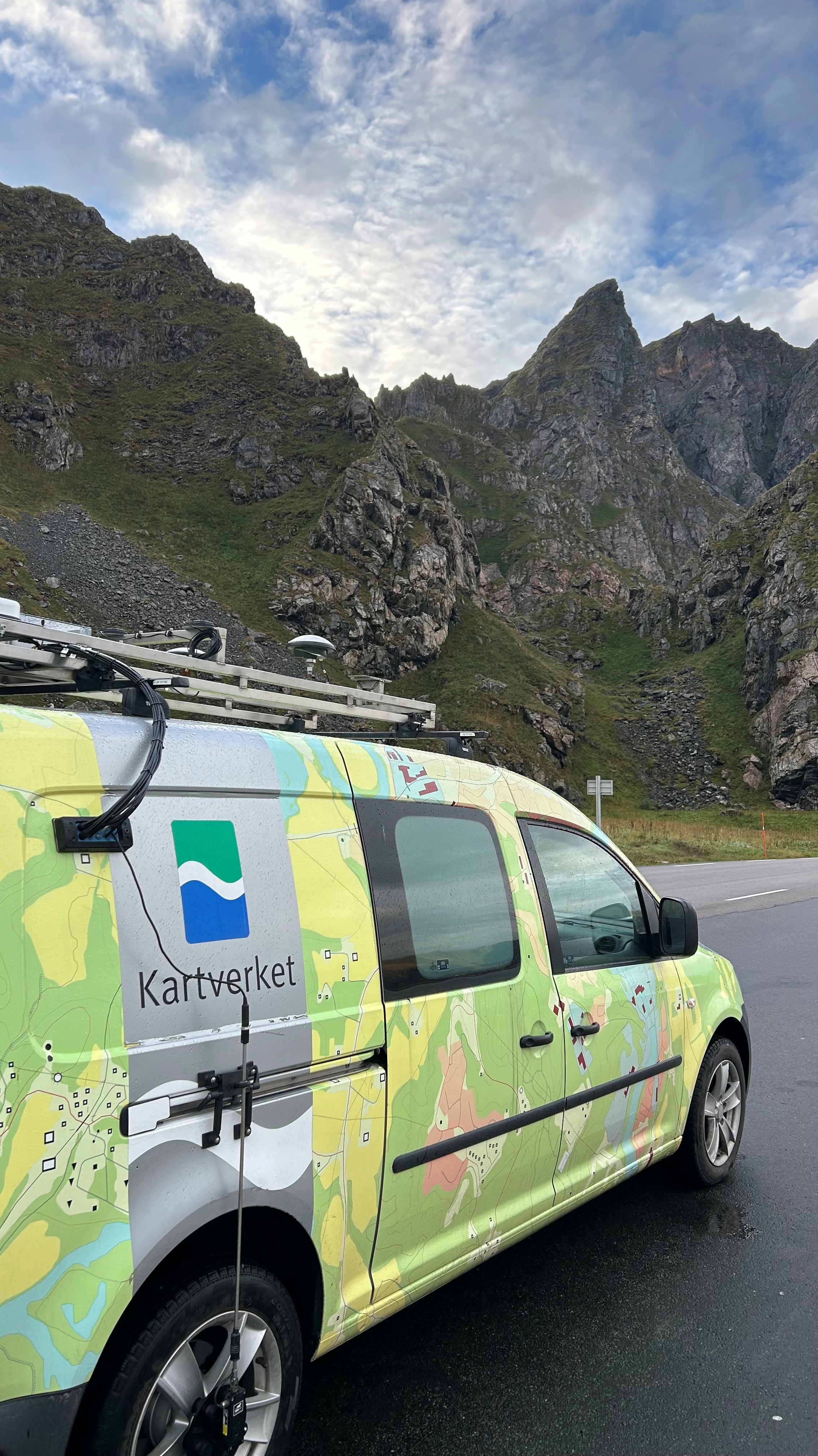 Varebil med Kartverket-logo og teknisk utstyr p&aring; taket foran bratt fjell.