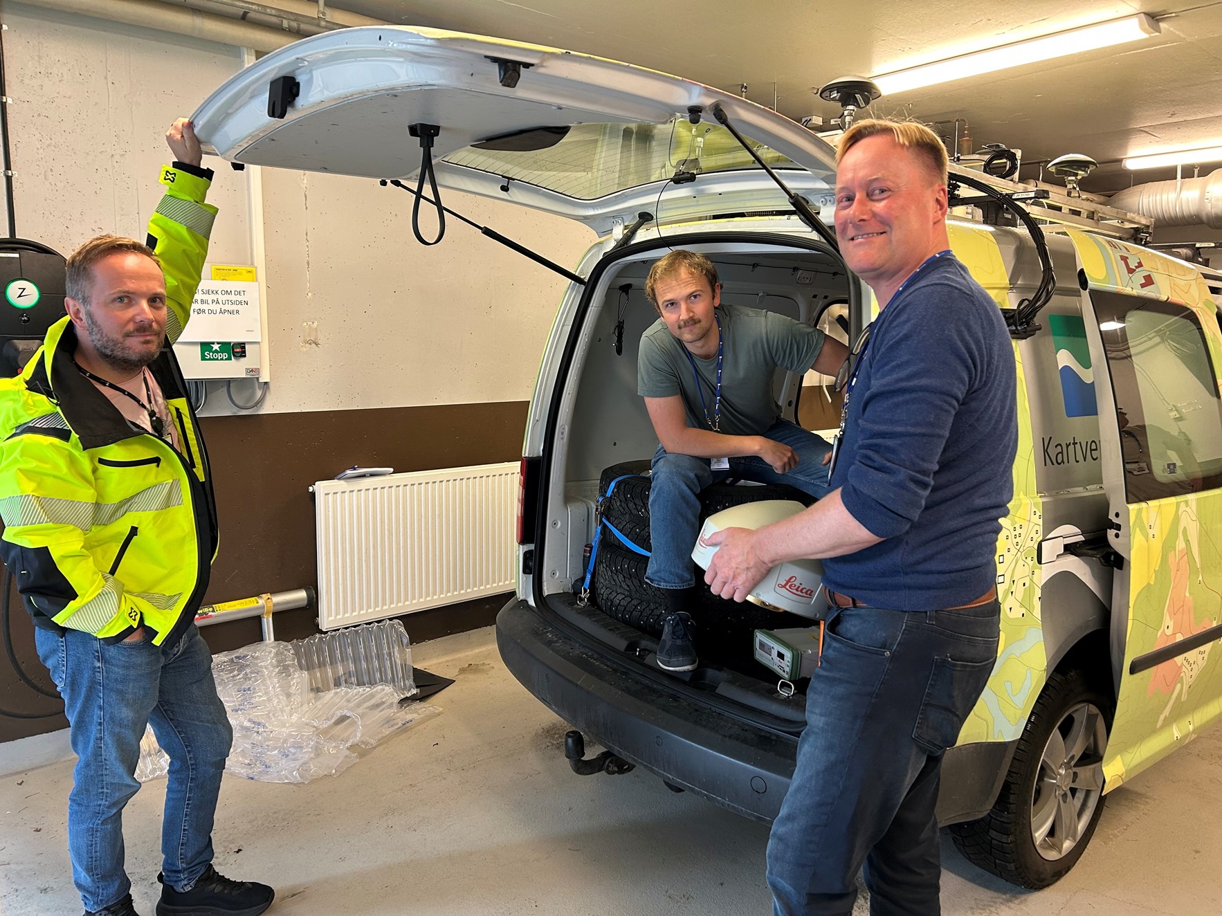 Tre ansatte i Kartverket pakker teknisk utstyr inn i en bil med Kartverket-logo.