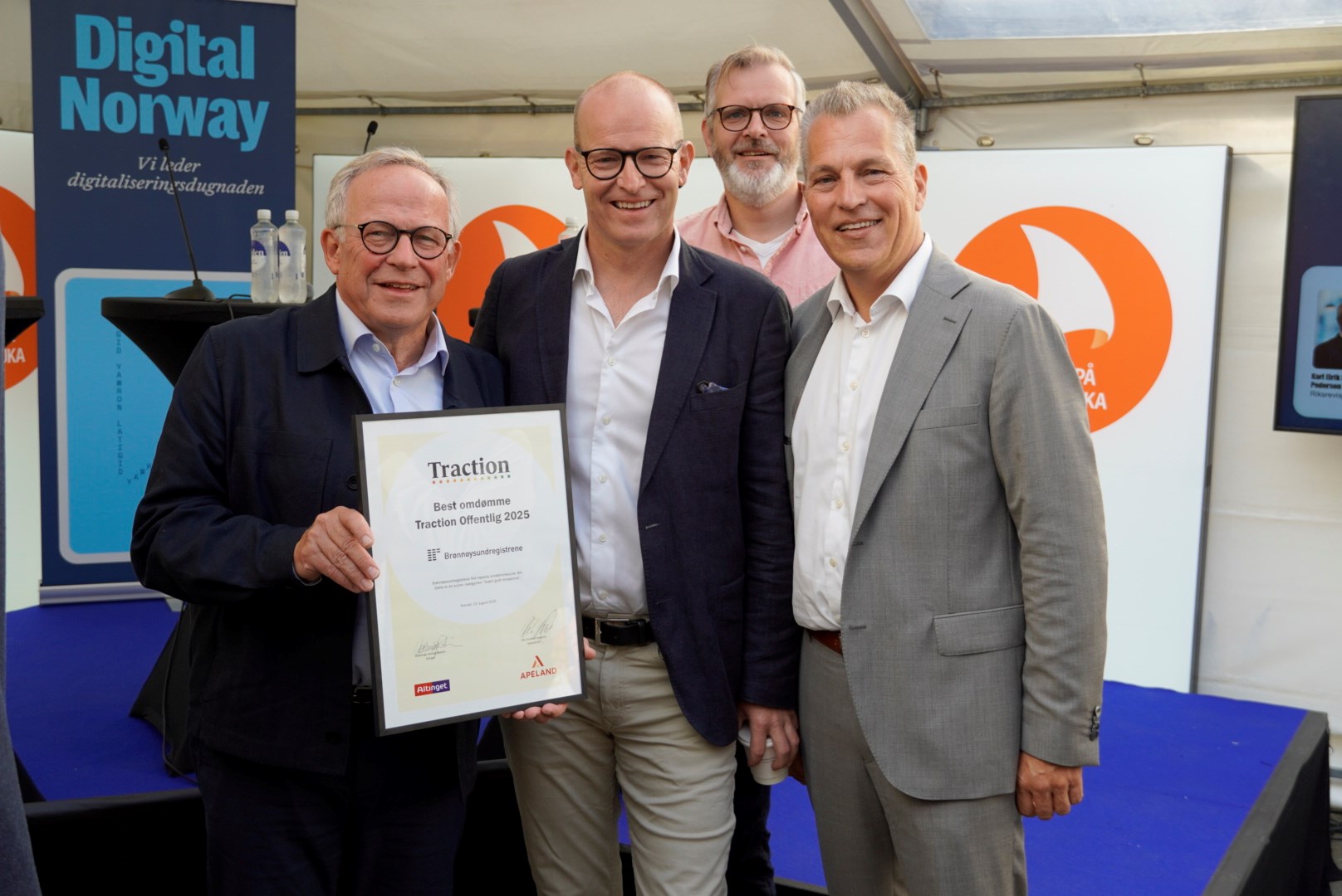 Fem middelaldrende menn i dress holder fram en plankett og smiler.