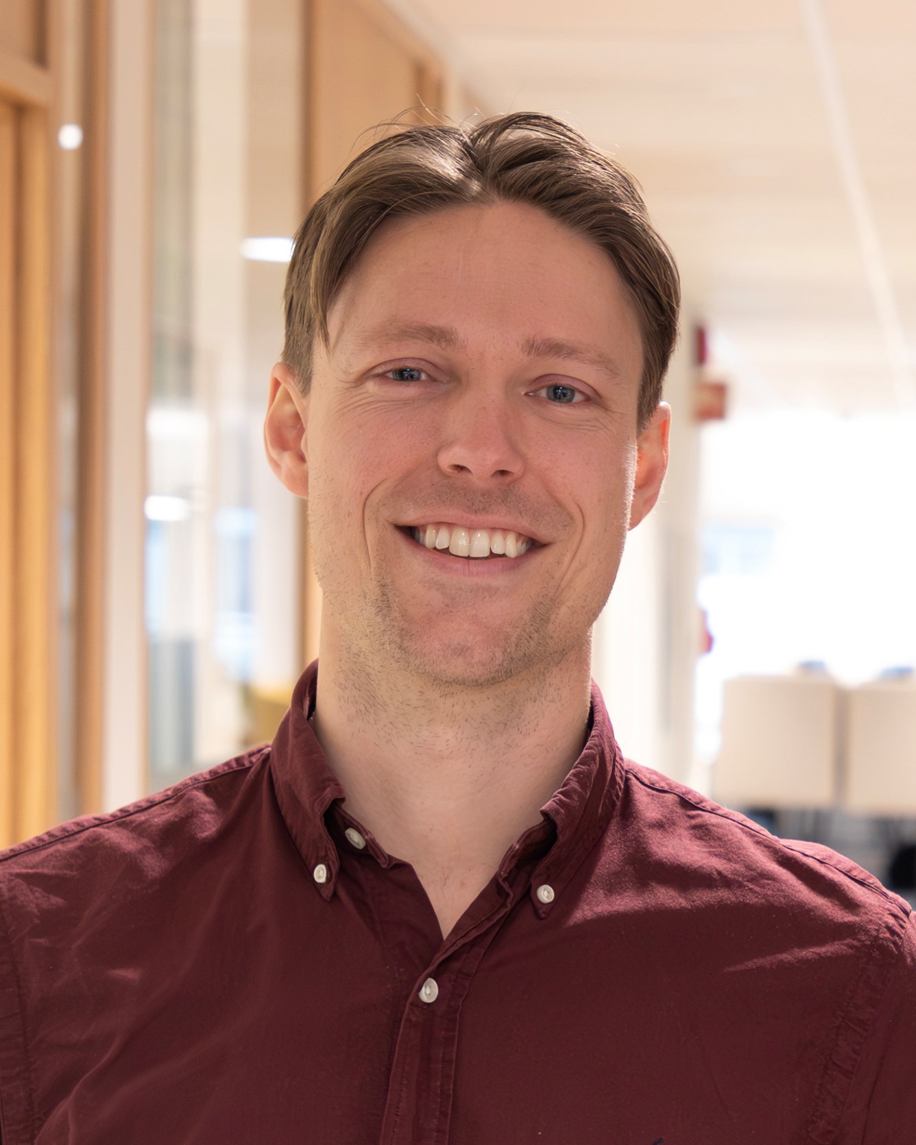 Mann i m&oslash;rker&oslash;d skjorte smiler til kamera.