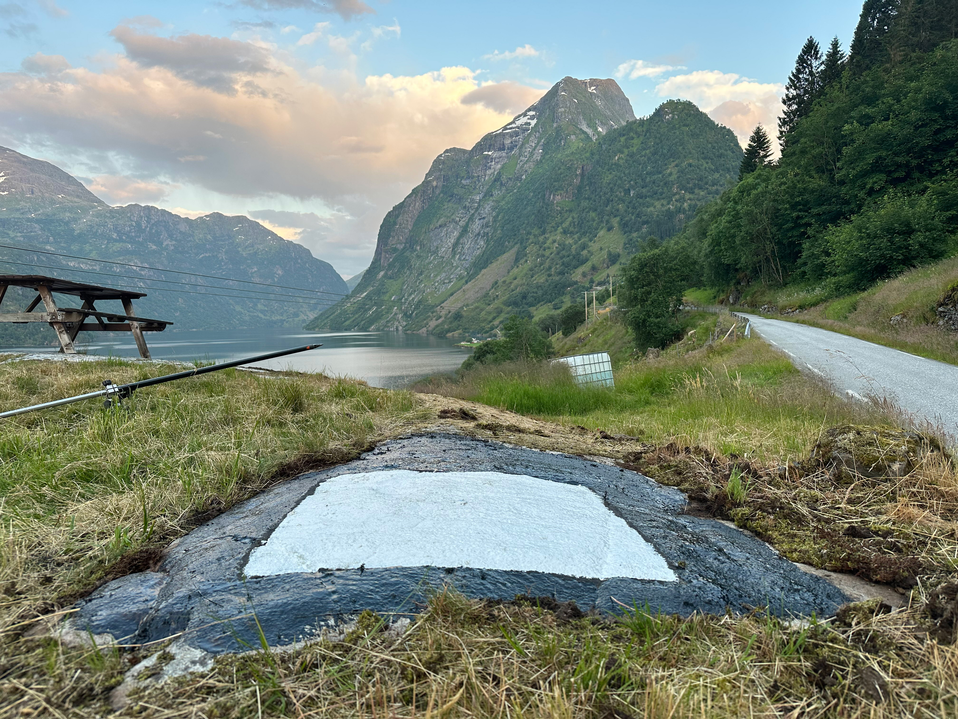 Fastmerke malt som en hvit firkant på en veiskulder, med bratte fjell i bakgrunnen.