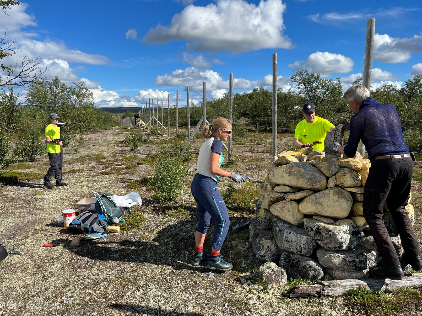 Mennesker restaurerer riksr&oslash;ys langs den finsk-norske riksgrensen. Et reinsdyrgjerde strekker seg i grensekorridoren.