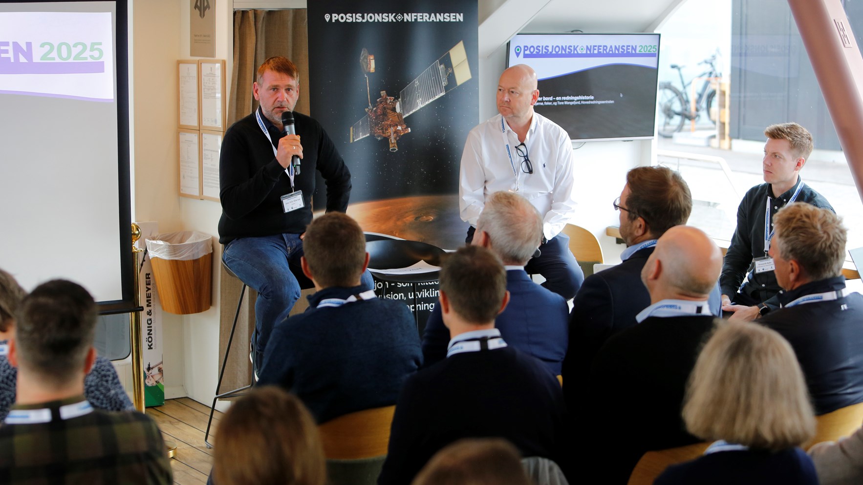Fisker Jon-Atle Bj&oslash;r&oslash;y og Tore Wangsfjord fra Hovedredningssentralen sitter foran publikum p&aring; Posisjonskonferansen. Bj&oslash;r&oslash;y snakker i en mikrofon.