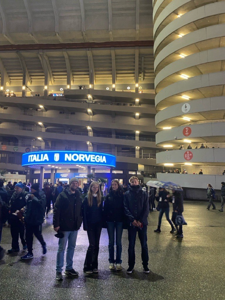 Fire personer st&aring;ende utenfor en fotballstadion. 