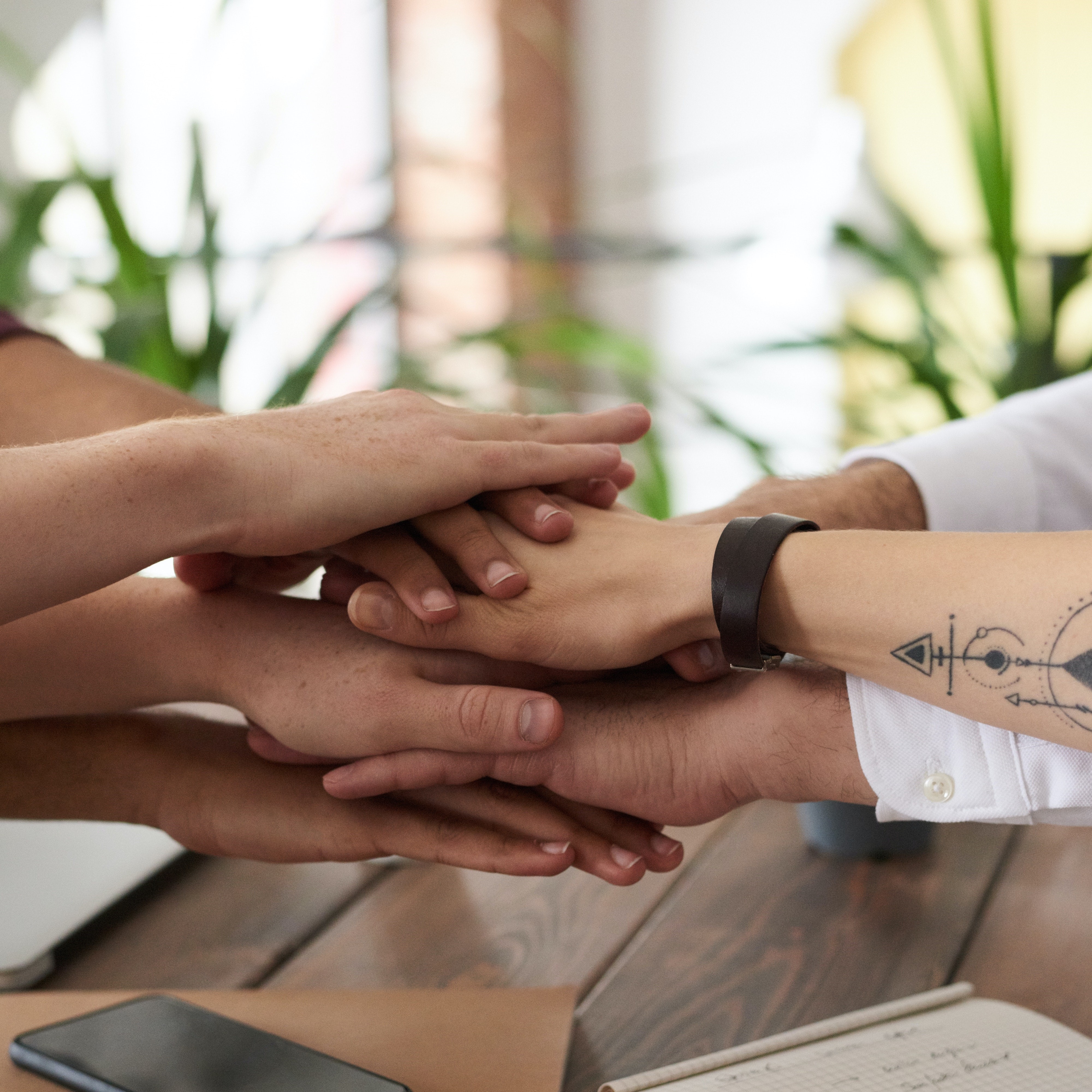Hender som holdes oppå hverandre i en stabel over et bord. Foto: Fauxels, Mostphotos.